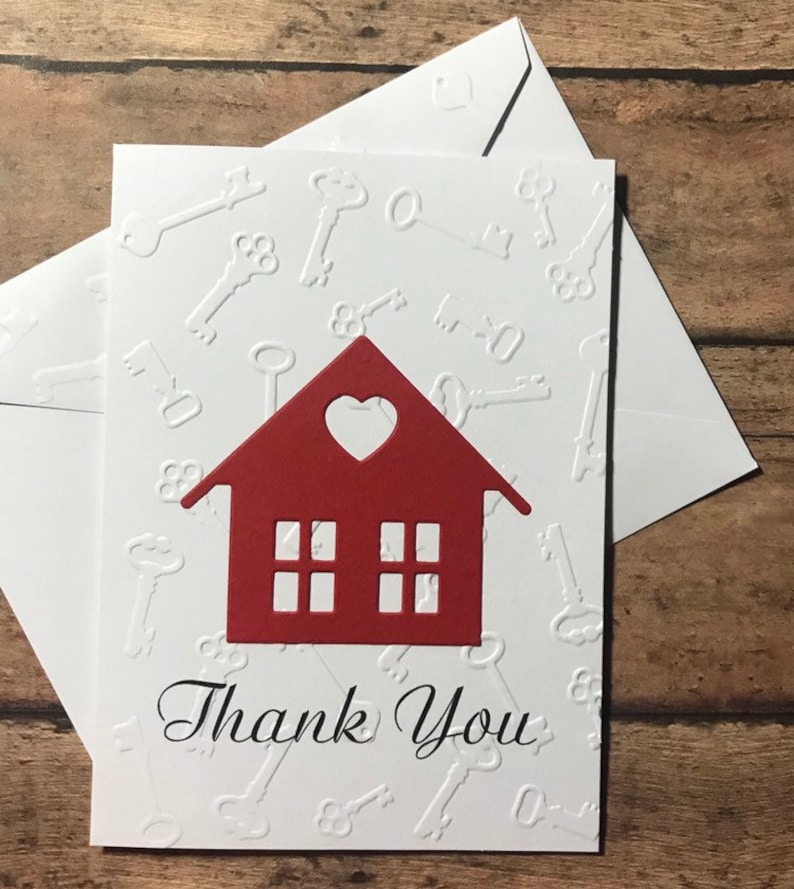 May include: A white card with a red house cutout and the words "Thank You" in black script. The background of the card is embossed with a pattern of keys.