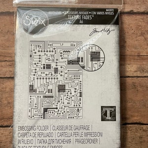 May include: A gray and white embossing folder with a circuit board design. The folder is packaged in a clear plastic bag with the brand name "Sizzix" and the text "Texture Fades" printed on it. The folder is labeled as "Embossing Folder", "Classeur de Gaufrage", "Carpeta de Repujado", "Cartella per le Impressioni in Rilievo", "Папка для тиснення", "Prägeordner", and "Placa de Textura e Emboss".