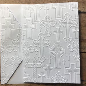 May include: White card stock with an embossed pattern of crosses. The crosses are in various sizes and styles, including simple crosses, ornate crosses, and Celtic crosses.