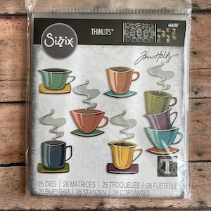 May include: A package of Sizzix Thinlits dies featuring various colorful coffee cup designs. The package includes 28 dies, with each cup design in a different color, such as green, orange, and blue. The package also includes the text "Jim Holtz".