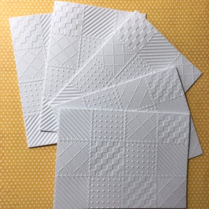 May include: Five white embossed cardstock sheets with different geometric patterns. Each sheet has a patchwork design with squares, diamonds, and stripes.
