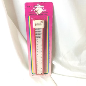 May include: A 4-in-1 multiplier school case in original pink packaging. The plastic pencil case features a white sliding top with a multiplication table and a ruler printed on the front. The packaging includes text reading 4 IN 1 MULTIPLIER SCHOOL CASE.