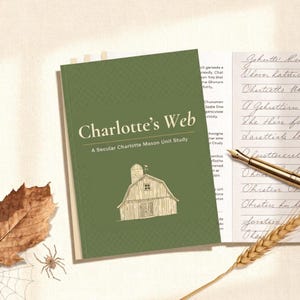 May include: A green book titled Charlotte's Web: A Secular Charlotte Mason Unit Study with a line drawing of a barn. Beside the book is a sheet of lined paper with handwritten cursive text and a gold fountain pen resting on the page.