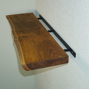 Puede incluir: Un estante de pared que presenta una tabla de madera con borde natural y un veteado marrón intenso. El estante está sostenido por un sistema de soporte de metal negro que incluye una barra horizontal con múltiples perforaciones circulares.