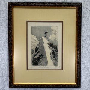 May include: A framed black and white etching depicting a mountain peak with a cross at the summit. The artwork is titled Grossglockner and features a dark brown textured frame with gold inner trim, set against a light beige matting board.