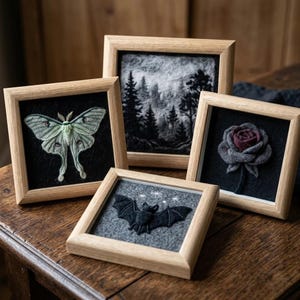 Pode incluir: Quatro molduras de madeira quadradas com arte em feltro. Uma apresenta uma mariposa verde-clara sobre fundo preto, uma uma paisagem florestal em preto e branco, uma uma rosa escura sobre preto e uma um morcego preto sobre cinza com estrelas.
