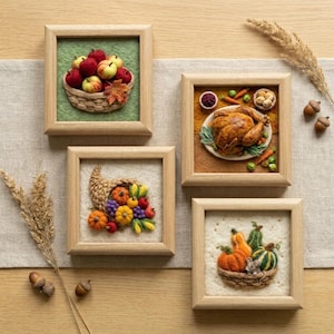 May include: Four square wooden frames containing needle-felted art. One shows a basket of red and yellow apples on green. Another features a roasted turkey on a plate with vegetables. A third displays a cornucopia of colorful produce. The last shows pumpkins in a basket.