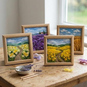 May include: Four square needle felted landscape pictures in light wood frames. The scenes depict rolling hills, a lavender field with a house, a golden wheat field, and paths through yellow and white wildflower meadows under blue skies with clouds.