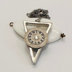 May include: A silver triangle pendant necklace with a white porcelain oval charm and a clock face with the word "WALTHAM" printed on it.