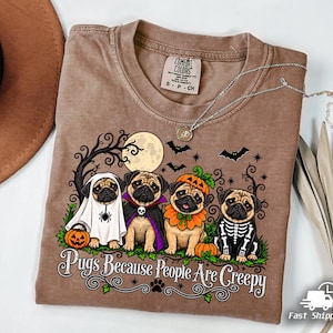 Może przedstawiać: Brązowy t-shirt z grafiką przedstawiającą cztery mopsy w kostiumach na Halloween, w tym ducha, wampira, dynię i szkielet. Napis głosi Pugs Because People Are Creepy. Wzór zawiera pełnię księżyca, nietoperze oraz nagie gałęzie drzew.