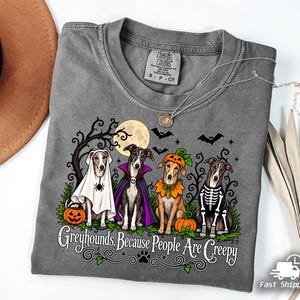 May include: A grey t-shirt featuring a graphic of four greyhounds in Halloween costumes, including a ghost, a vampire, a pumpkin, and a skeleton. The text reads, Greyhounds, Because People Are Creepy, set against a background of trees, bats, and a moon.