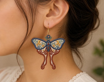 May include: A large moth-shaped dangle earring featuring intricate embroidery in shades of navy blue, rust orange, and cream. The design includes celestial moon motifs, floral patterns, and a gold-toned metal hook for attachment to the earlobe.
