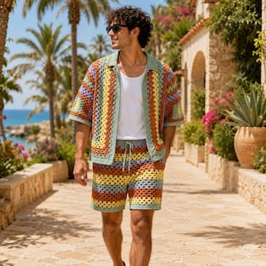 Può includere: Una camicia a maniche corte in crochet con bottoni e pantaloncini coordinati con coulisse, caratterizzati da un motivo a piastrelle granny multicolore nei toni del verde salvia, giallo, arancione, viola e blu, indossati sopra una t-shirt bianca.