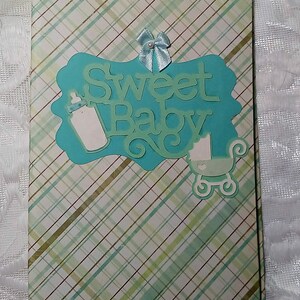 May include: A blue and green scrapbook with the words "Sweet Baby" on the front. The scrapbook has a plaid pattern and a blue bow.