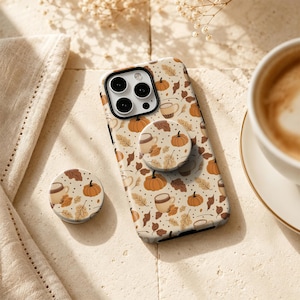 May include: A cream-coloured smartphone case and a matching circular phone grip featuring a repeating pattern of orange pumpkins, brown coffee mugs, and tan autumn leaves on a background with small brown dots, designed for a triple-lens camera.