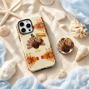 May include: A smartphone case and a matching circular phone grip featuring a cartoon turkey wearing a pilgrim hat, surrounded by autumn leaves and the text Happy Thanksgiving on a cream-colored background with a subtle polka dot pattern.