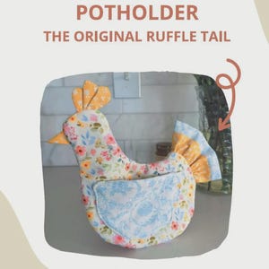 May include: A chicken-shaped potholder featuring a floral pattern in yellow, pink, and blue, with a solid blue wing-shaped pocket and a ruffled tail. Text on the image reads: LIBBY CHICKEN POTHOLDER THE ORIGINAL RUFFLE TAIL COZY COOP COTTAGE @LITTLETHINGSWITHJULIE.