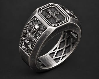 May include: A silver-toned metal ring featuring an octagonal top plate with an embossed cross. The sides of the ring display a detailed relief of a figure with long hair holding a heart, and the band has an open lattice cutout design.