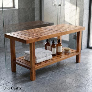 May include: A rectangular wooden shower bench with a slatted top and a lower shelf. The bench features four sturdy legs and is holding a stack of white folded towels, three brown amber-colored bottles with labels, and a small round wooden brush.