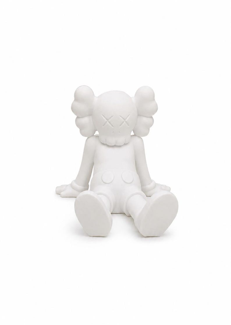 Op de afbeelding: Een witte, zittende figuur met een opvallend ontwerp. De figuur heeft grote, afgeronde oren, gekruiste ogen en een zittende houding met uitgestrekte armen en benen. De algehele esthetiek is minimalistisch en modern, met een gladde, matte afwerking.