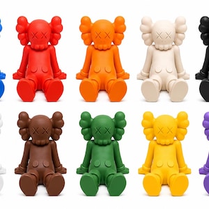Op de afbeelding: Een verzameling van tien kleurrijke vinylfiguren in verschillende kleuren, waaronder blauw, rood, oranje, cr&egrave;me, zwart, wit, bruin, groen, geel en paars. Elke figuur heeft een kenmerkend ontwerp met gekruiste ogen en een afgeronde kop.