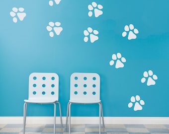 May include: Two white chairs with a cut-out design sit in front of a light blue wall with white paw prints.