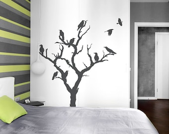 May include: A dark gray tree silhouette with perched and flying crows decorates a white wall. The bedroom features a gray bedspread, a green pillow, and a striped accent wall with gray and lime green stripes. A white pendant light hangs from the ceiling.