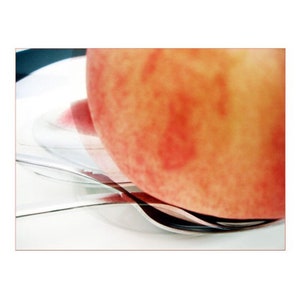 May include: A close-up of a peach with a red blush, resting on a silver spoon. The peach is slightly out of focus, while the spoon is in sharp focus.