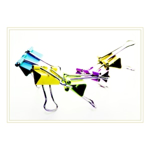 May include: Four colorful binder clips interlocked together. The clips are blue, yellow, green, and purple.