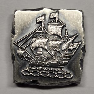 May include: A square silver-toned metal plaque featuring a raised relief design of a sailing ship with multiple masts and sails. The ship is depicted moving across stylized waves. The edges of the metal piece are irregular and textured.