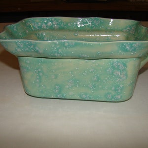 May include: A two-piece ceramic serving dish set. The set features a rectangular base with a handle and a scalloped-edge top, both in a speckled turquoise glaze. The dish is suitable for serving food.