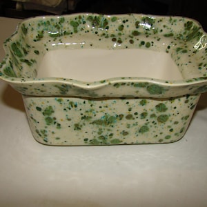 May include: A rectangular ceramic dish with a scalloped rim. The dish is off-white with green and yellow speckles. The interior is a solid off-white color. The dish is likely used for serving or display.