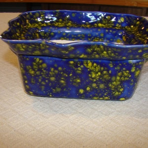 May include: A rectangular ceramic planter with a wavy rim, glazed in a vibrant blue with speckled yellow accents. The planter is designed with a two-tiered structure, suitable for indoor or outdoor use.