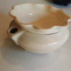 May include: Cream-colored ceramic oil warmer with a scalloped dish on top. The base is round with a small spout. The warmer is designed to hold essential oils and create a relaxing atmosphere. A decorative item for the home.