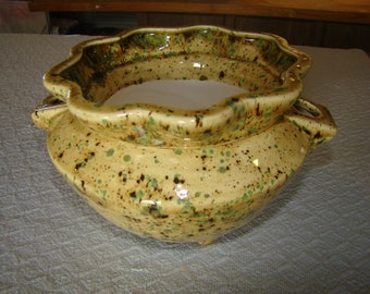 May include: A ceramic planter with a scalloped rim and two handles. The planter has a speckled, light yellow glaze with brown and green accents. The interior is white.