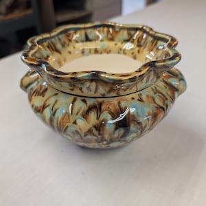 May include: A ceramic bowl with a scalloped rim and a rounded body, featuring a marbled glaze pattern in shades of brown, tan, and light blue. The interior of the bowl is smooth and off-white, contrasting with the decorative exterior finish.