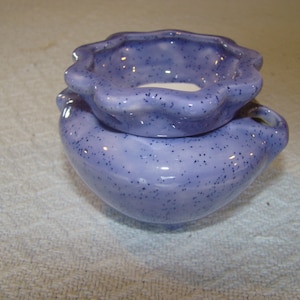 May include: A two-piece ceramic oil warmer in a speckled lavender color. The base is heart-shaped with a small handle, and the top is a smaller, scalloped-edge dish. The warmer is designed to hold scented oils and a tea light.