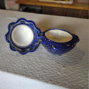 May include: Two-piece ceramic serving dish set. The pieces are a deep blue with yellow speckles and a scalloped edge. The interior is white. The dish has two small handles.