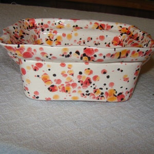 May include: A two-piece ceramic dish set with a speckled pattern. The set features a rectangular base and a flared top, both adorned with red, orange, and black spots on a white background. The dish set is likely for serving or display.