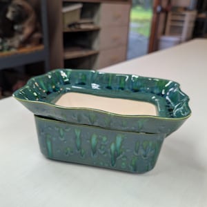 May include: A rectangular ceramic planter with a wavy, scalloped rim. The exterior features a glossy, mottled glaze in shades of deep forest green and teal with vertical drip patterns. The interior base is a smooth, matte, off-white ceramic surface.