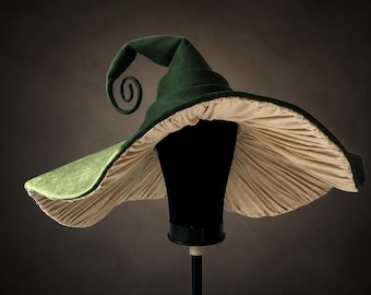 Può includere: Un cappello a tesa larga caratterizzato da un esterno verde bosco profondo con una consistenza liscia e una corona appuntita e ricurva. La parte inferiore della tesa è foderata con un tessuto color crema, densamente arricciato.