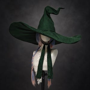 May include: A dark forest green pointed hat with a wide, flexible brim and a tall, slightly curved crown. The hat features two long, matching green fabric ties hanging down from the base, designed to be secured under the chin for a snug fit.