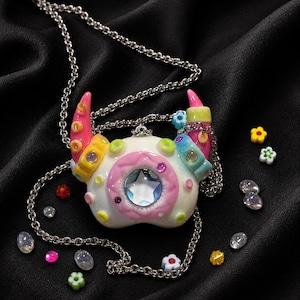 May include: A pendant necklace featuring a white, horn-shaped charm with pink, yellow, and blue accents. The center displays a large, faceted star-shaped gem surrounded by a pink ring. The charm is attached to a silver-toned metal chain.