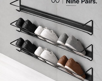 Könnte beinhalten: Ein schwarzes Wand-Schuhregal aus Metall mit drei horizontalen Ebenen. Das Regal enthält verschiedene Schuhe, darunter schwarze, weiße, graue und braune Paare. Der Text auf dem Bild lautet: Hold up to Nine Pairs. Drahtrahmen-Design.