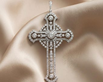 May include: A diamond-encrusted cross pendant with a detailed design. The pendant features a large central diamond and numerous smaller diamonds, set in a silver or white gold metal. The cross is displayed on a satin fabric.
