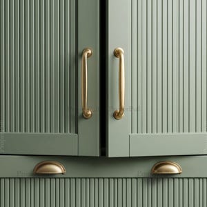 May include: Sage green cabinet doors and drawers featuring a vertical fluted texture. The cabinetry is accented with brushed brass hardware, including two long vertical pull handles on the doors and two semi-circular cup pulls on the drawers.