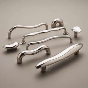 May include: A collection of polished silver-toned metal cabinet hardware, including various curved drawer pulls and two distinct knobs. Each piece features a smooth, reflective finish and organic, flowing shapes with the text PROPERPULL visible.