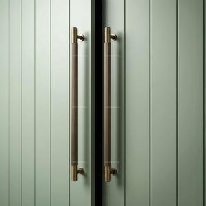 Puede incluir: Dos tiradores de armario cilíndricos y largos de bronce oscuro con una textura acanalada vertical. Cada tirador está montado en una puerta de color verde salvia con paneles verticales y dos soportes metálicos circulares con el texto PROPERPULL.