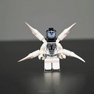Può includere: Una minifigure Lego di Spider-Man bianca e nera con quattro estensioni bianche a forma di ala appuntita. La figura ha una testa nera con un disegno a ragnatela bianca e un disegno a ragnatela nera sul petto.