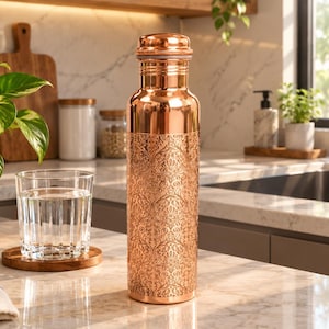 Peut inclure: Une bouteille d'eau cylindrique en cuivre avec une finition métallique polie et un motif damassé complexe en relief couvrant les deux tiers inférieurs du corps. La bouteille possède un col lisse et arrondi ainsi qu'un bouchon en cuivre assorti.